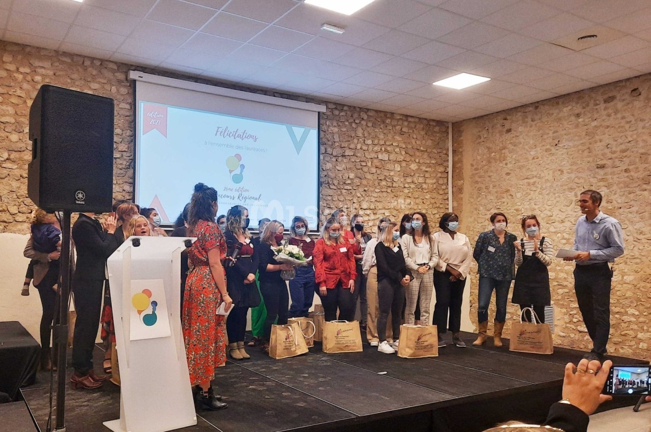 Un groupe de personnes sur scène lors d'une remise de prix dans une salle avec un mur en pierre et un écran de projection.