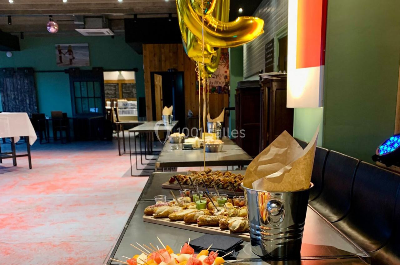 Buffet avec amuse-bouches variés, brochettes de fruits et décorations, dans une salle de réception lumineuse.