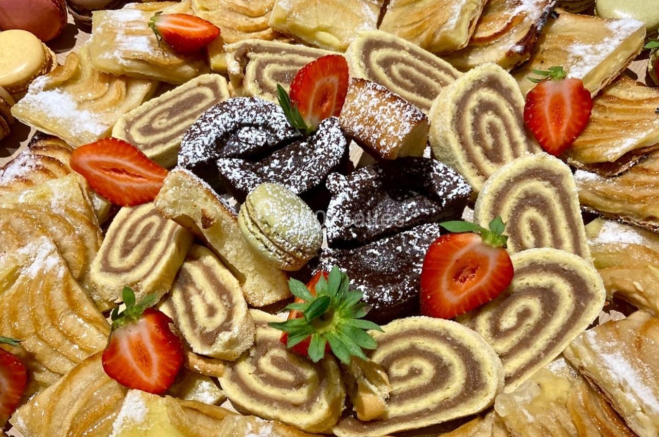 Assortiment de pâtisseries variées avec des roulés, des macarons, des fraises et des biscuits saupoudrés de sucre glace.