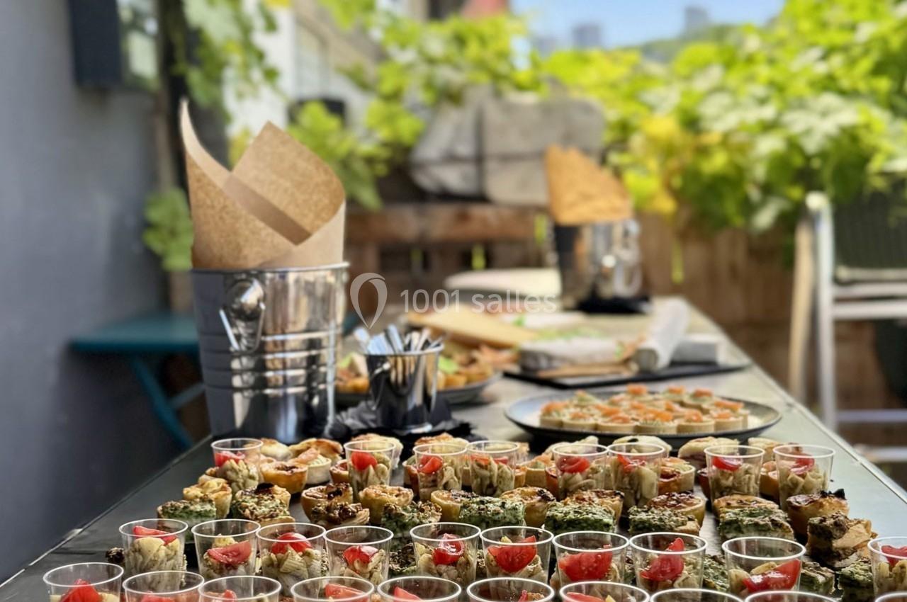Buffet en extérieur avec verrines et amuse-bouches variés, disposés sur une table entourée de verdure.