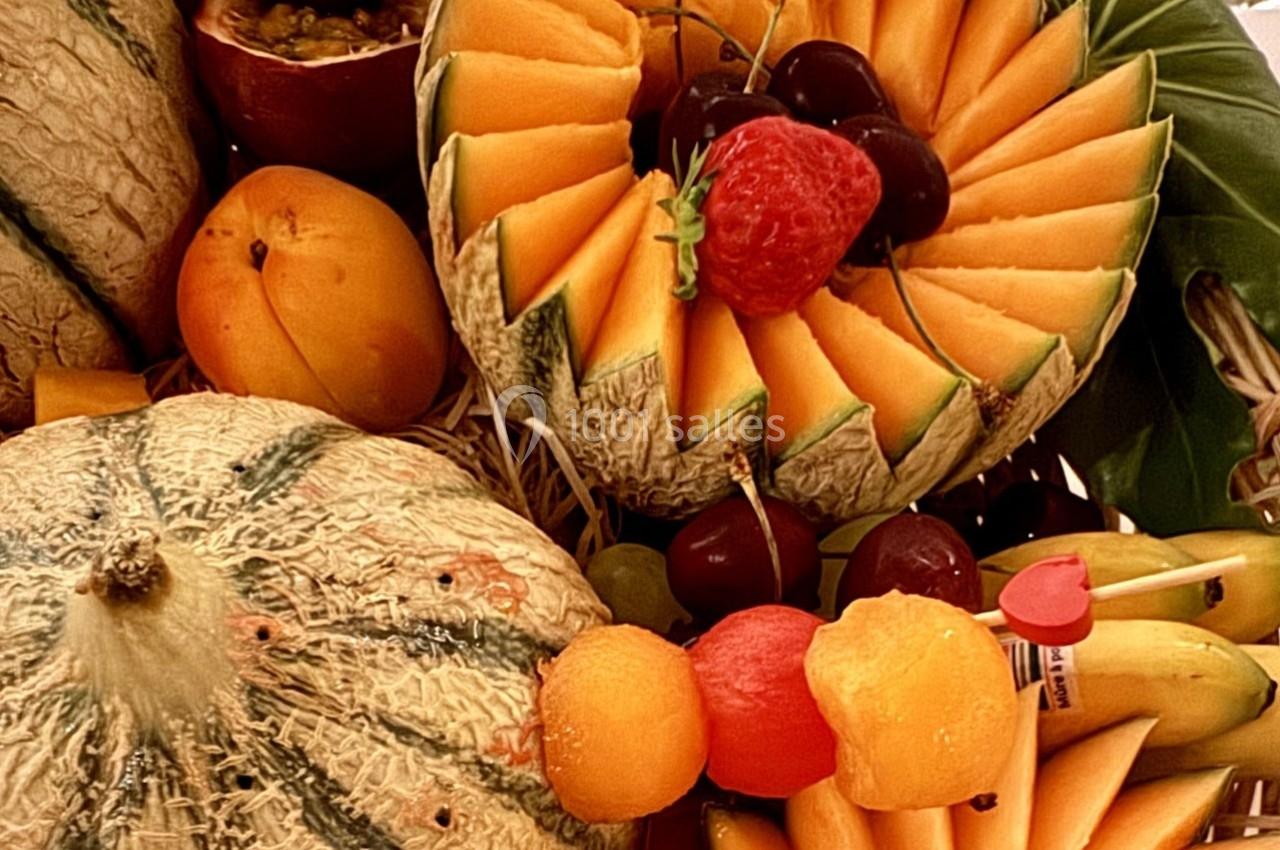Plateau de fruits variés avec melon sculpté, raisin, fraise, abricots, bananes et brochettes de billes de fruits.