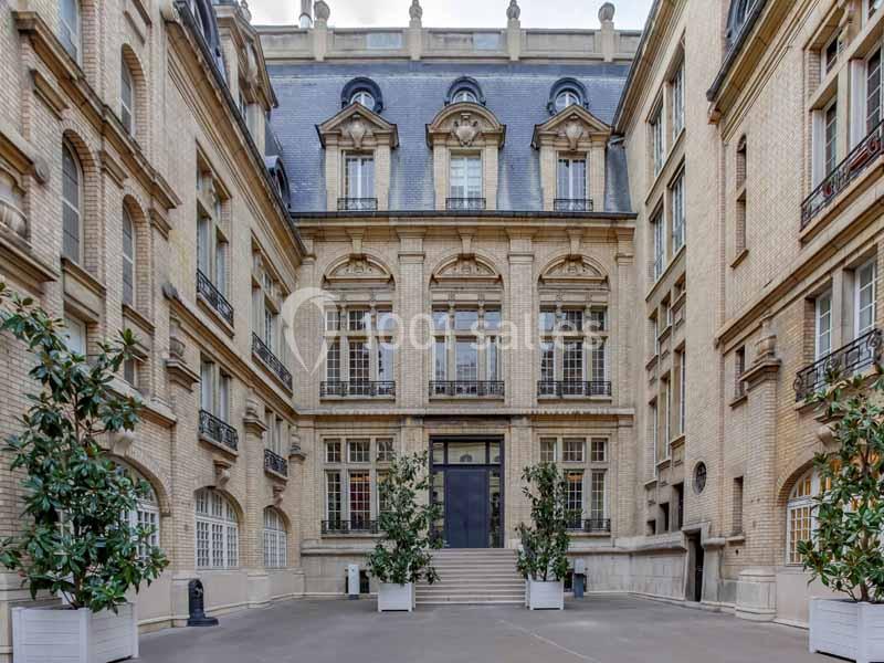 Cour intérieure d'un bâtiment en briques avec des fenêtres à balcons, un escalier central et des plantes en pots.