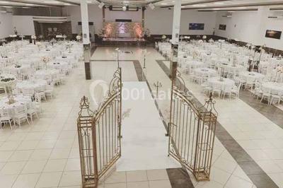 Salle de réception décorée avec des fleurs et éclairages roses, scène équipée de matériel audio en arrière-plan.