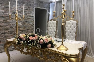 Salle de réception décorée avec des fleurs et éclairages roses, scène équipée de matériel audio en arrière-plan.