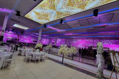 Salle de réception décorée avec des fleurs et éclairages roses, scène équipée de matériel audio en arrière-plan.