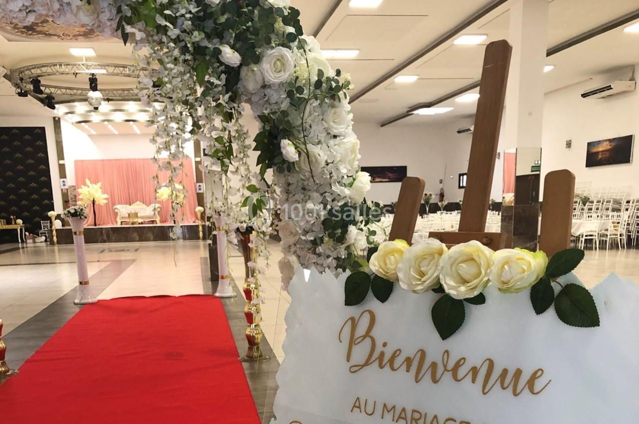 Arche florale blanche et panneau de bienvenue décoré de roses jaunes à l'entrée d'une salle de mariage avec tapis rouge.
