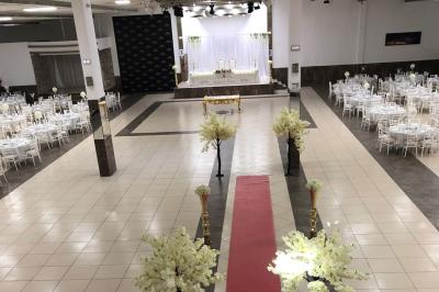 Salle de réception décorée avec des fleurs et éclairages roses, scène équipée de matériel audio en arrière-plan.