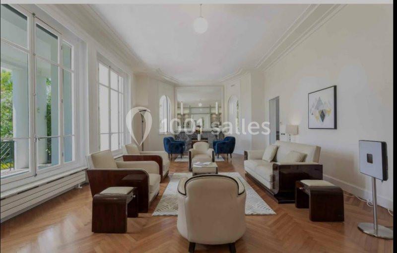 Salon lumineux avec parquet en bois, mobilier moderne, grandes fenêtres et vue sur une cuisine ouverte.