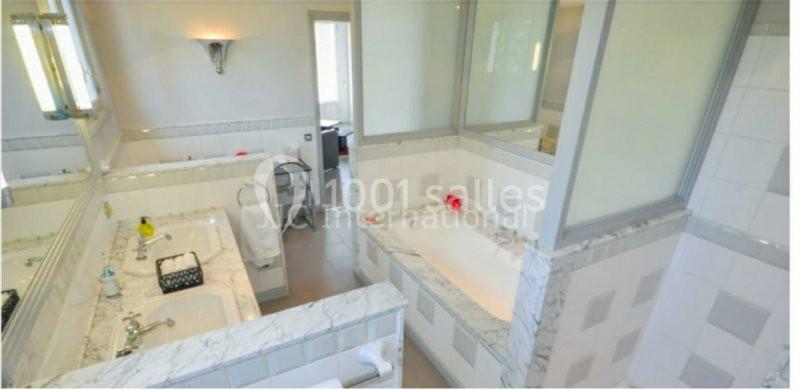Salle de bain lumineuse avec baignoire encastrée, double vasque en marbre et miroirs sur les murs.