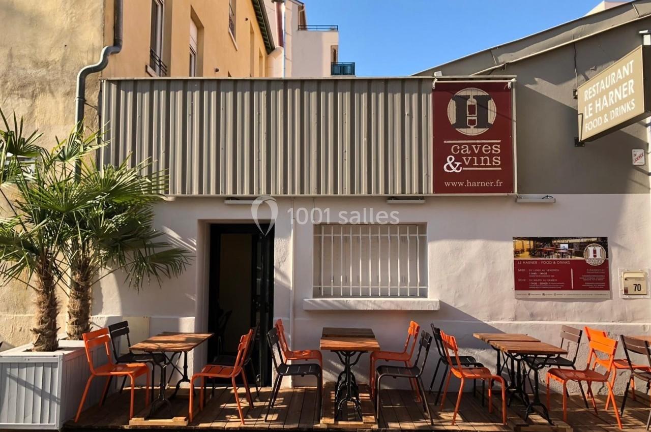 Façade d'un restaurant avec terrasse en bois, chaises orange et enseigne indiquant ’Caves & Vins’.