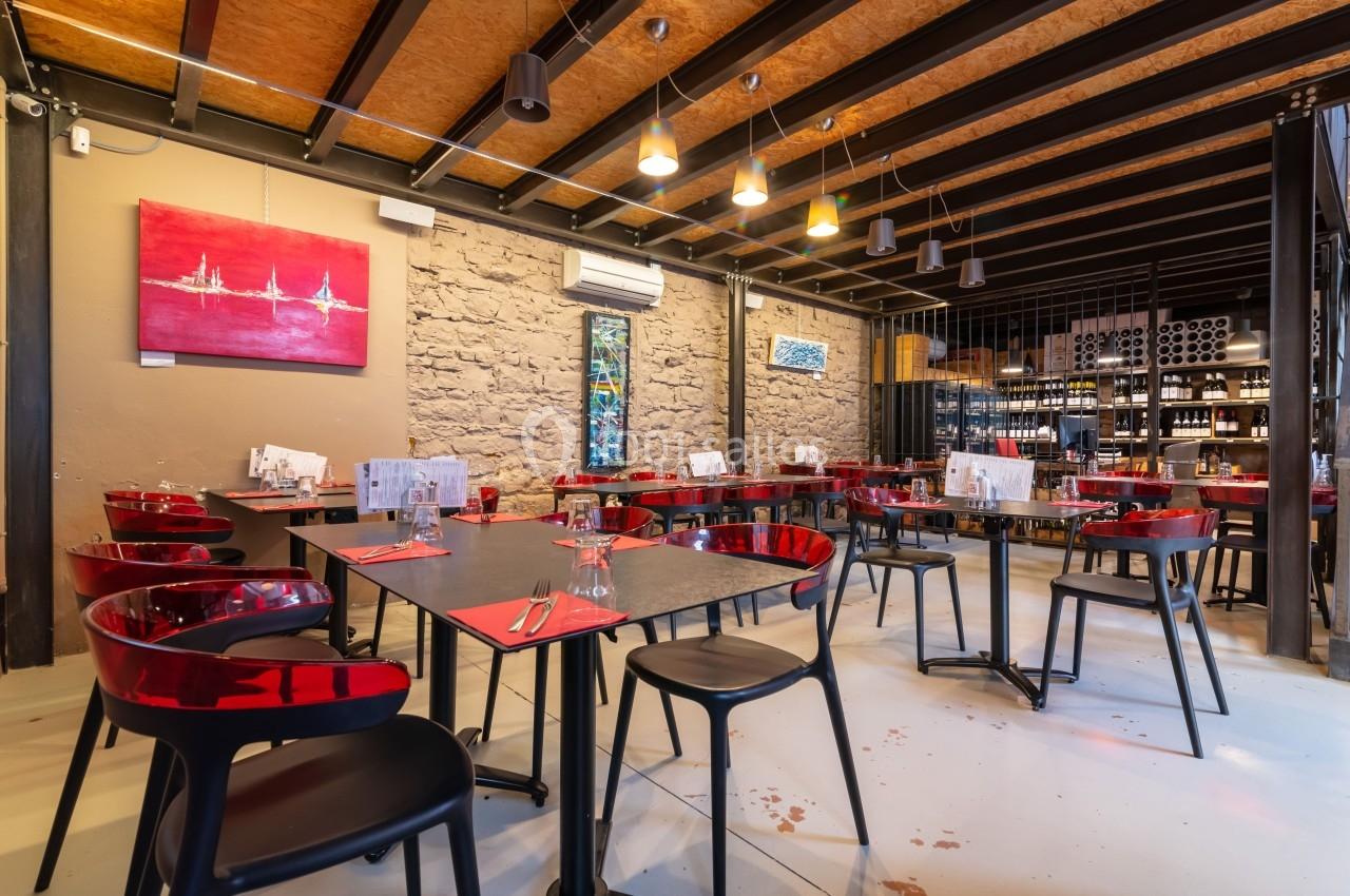 Salle de restaurant moderne avec tables noires, chaises rouges transparentes et décoration murale contemporaine.
