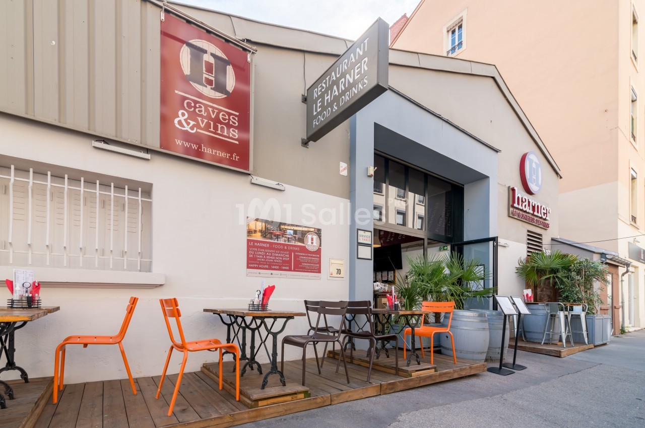 Terrasse extérieure d'un restaurant avec tables, chaises colorées et enseignes visibles sur une façade beige.