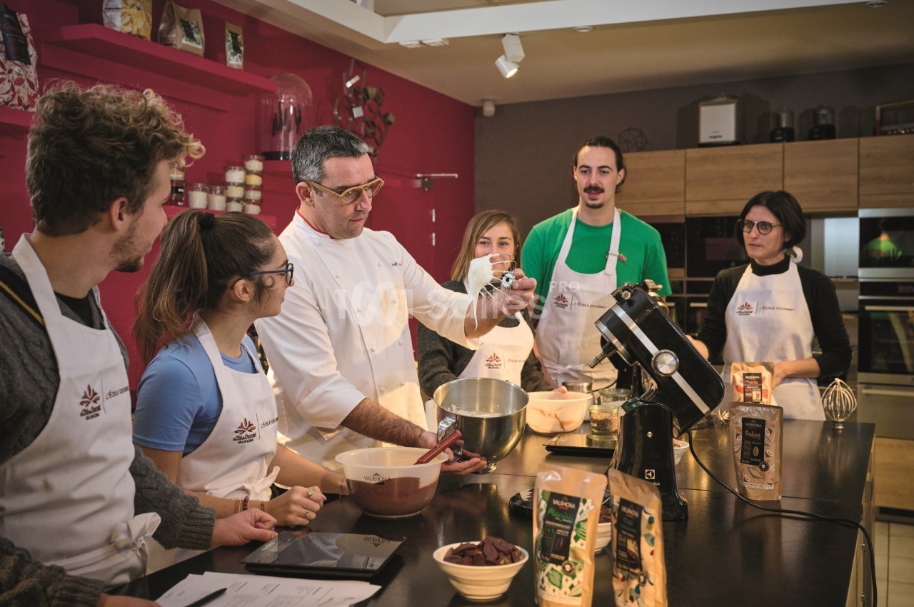 Un chef pâtissier enseigne à un groupe de personnes en tabliers autour d'un plan de travail avec des ingrédients.