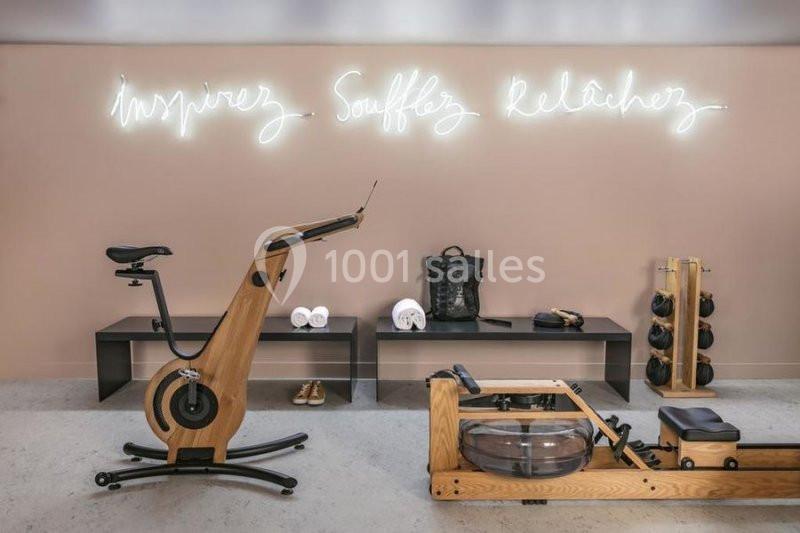 Salle de sport avec vélo en bois, rameur, banc, accessoires et néons affichant ’Inspirez, Soufflez, Relâchez’.