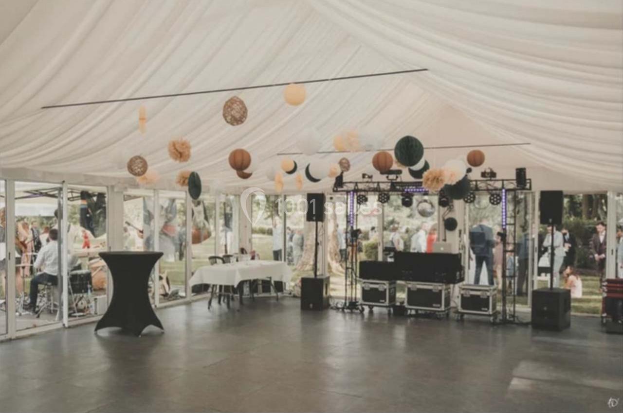 Intérieur d'une tente de réception décorée avec des lanternes suspendues, tables et matériel de sonorisation installés.