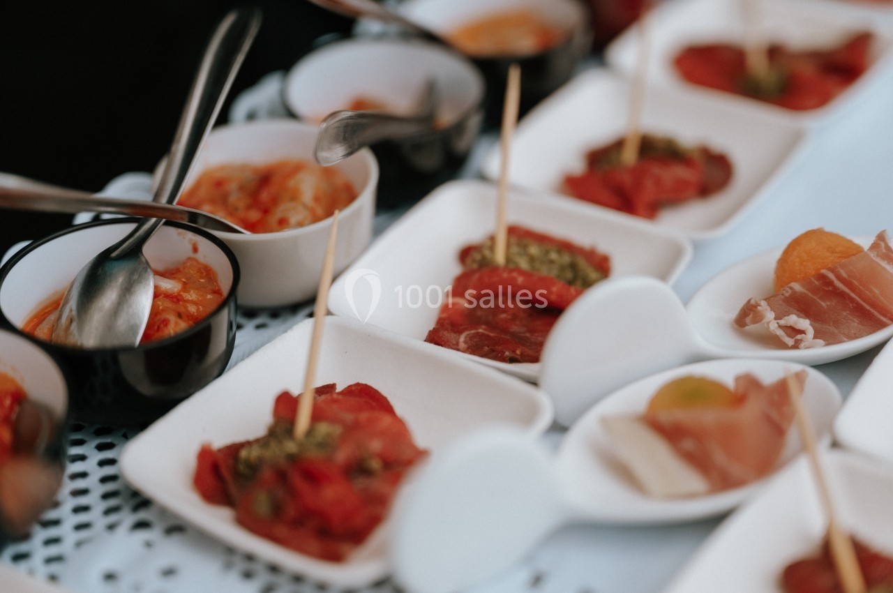 Assortiment de petites assiettes contenant des charcuteries, légumes marinés et condiments, disposées sur une table.