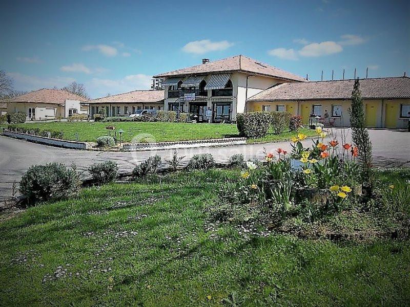 Bâtiment à un étage entouré de pelouses, parterres fleuris et allées pavées, sous un ciel dégagé.