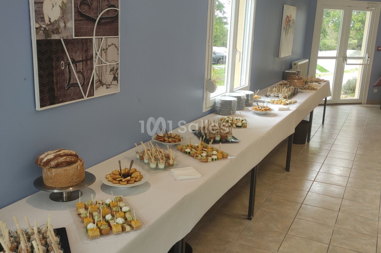 Buffet avec divers amuse-bouches, pains et desserts disposés sur une longue table dans une salle lumineuse.