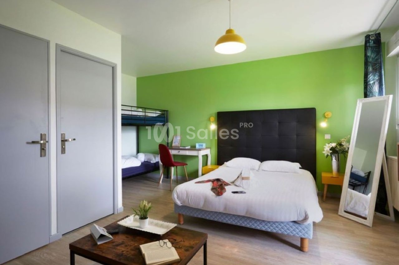 Chambre lumineuse avec lit double, lits superposés, bureau, miroir sur pied et murs verts.