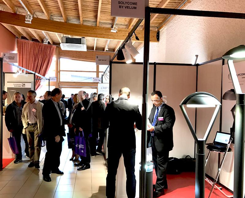 Des personnes discutent dans un salon professionnel, entourées de stands exposant des produits sous un éclairage intérieur.