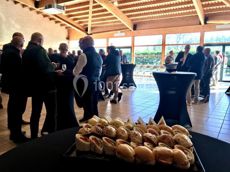 Plateau de petits sandwichs en premier plan dans une salle lumineuse où des personnes discutent debout autour de tables…