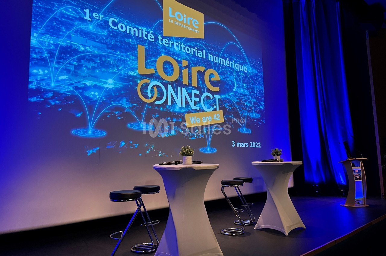 Salle de conférence avec des tables hautes et un écran affichant un événement numérique intitulé ’Loire Connect’.