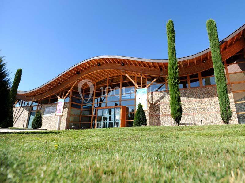 Façade d'un bâtiment moderne avec une structure en bois, des murs en pierre et des arbres devant une pelouse.