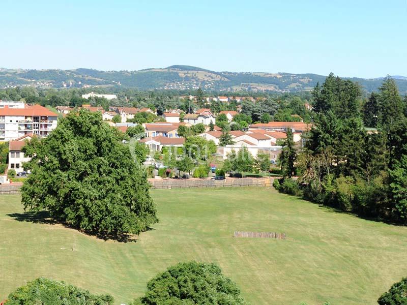 Vue d'un parc avec une grande pelouse, des arbres, des habitations en arrière-plan et des collines à l'horizon.