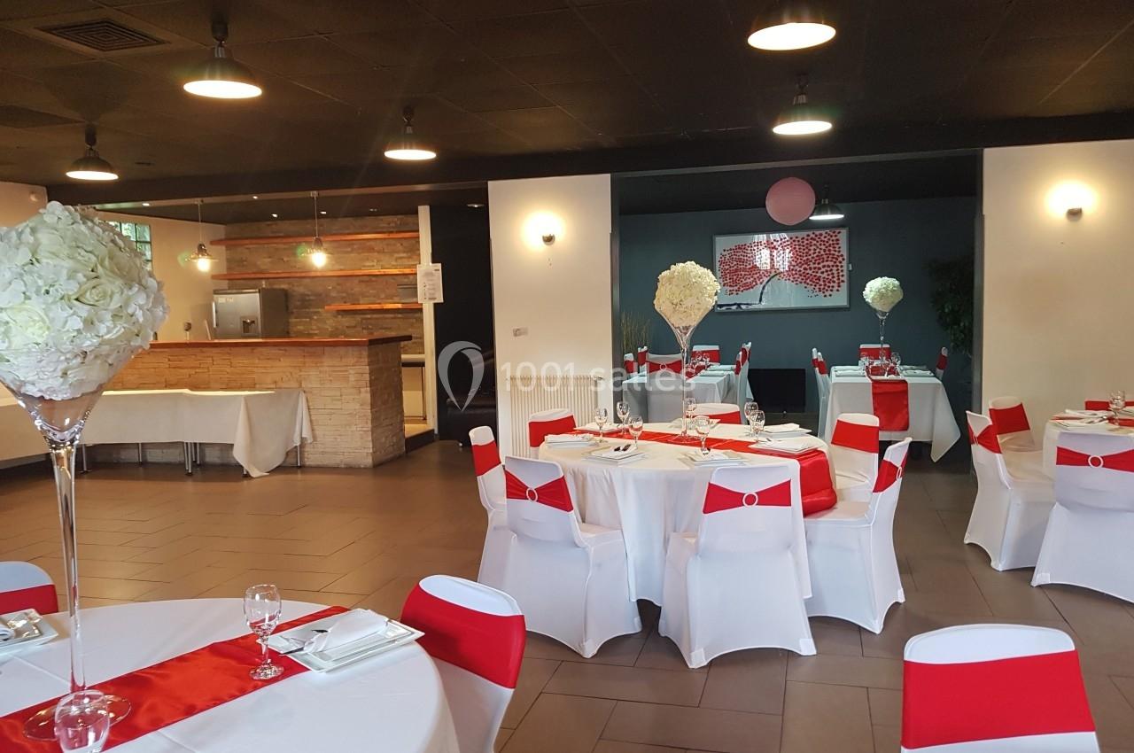 Salle de réception décorée avec des tables rondes, nappes blanches, chemins de table rouges et centres de table floraux.