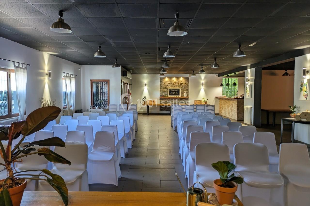 Salle de réception lumineuse avec des rangées de chaises blanches, un comptoir en bois et des plantes en décoration.