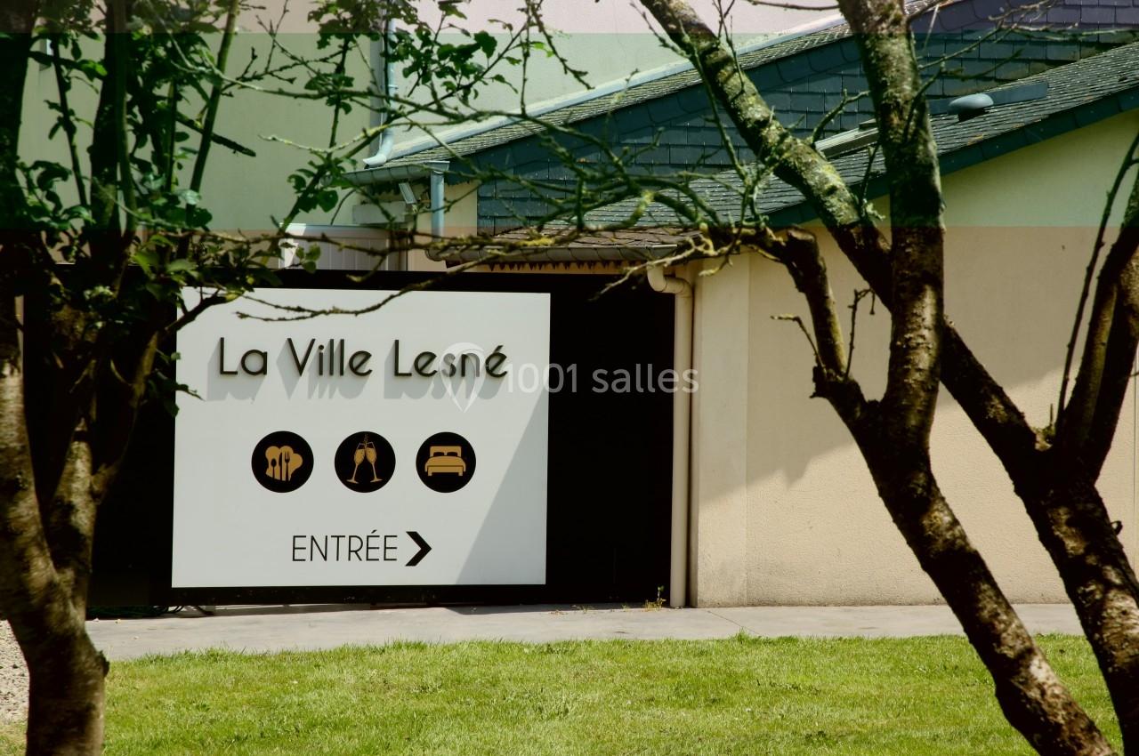 Panneau indiquant l'entrée d'un bâtiment nommé ’La Ville Lesné’ avec des pictogrammes de services et une flèche…