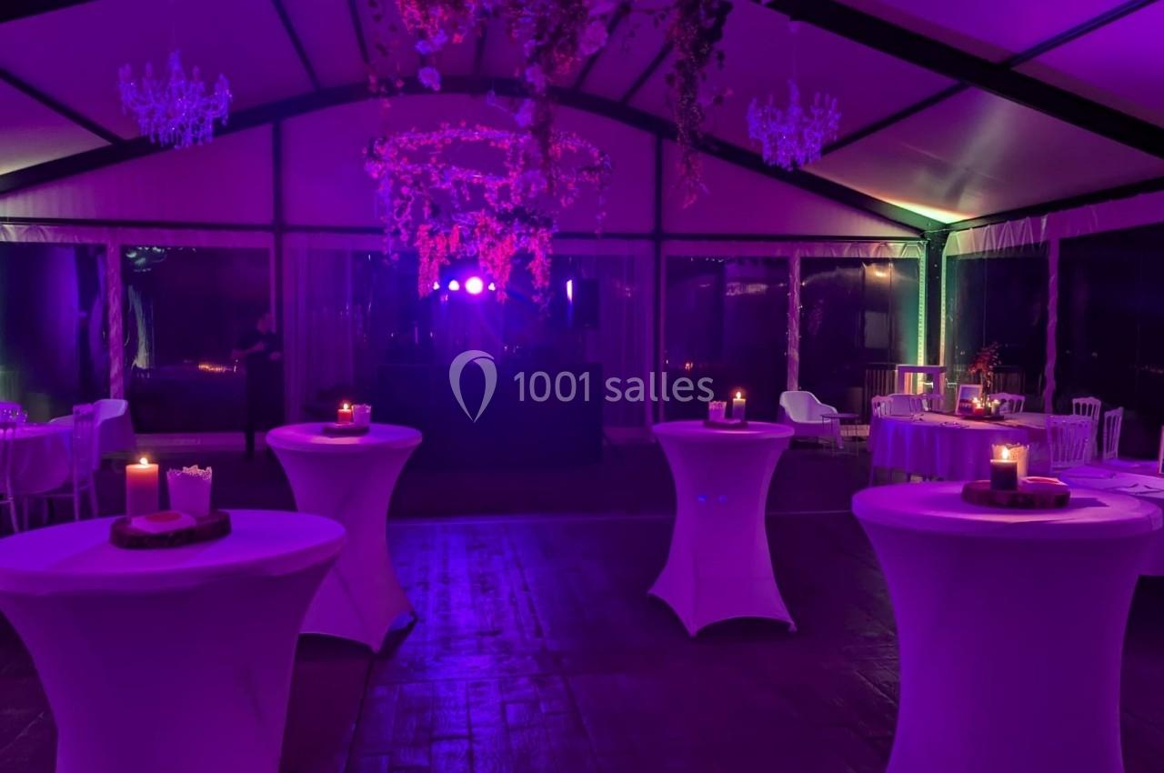 Salle de réception éclairée par des lumières violettes, avec tables hautes décorées de bougies et un espace central dégagé.