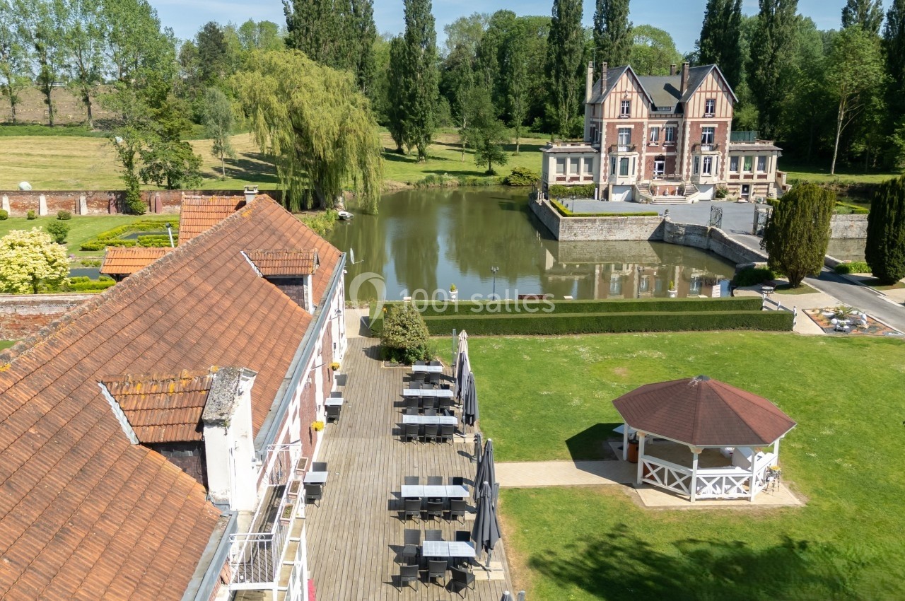 Vue aérienne d'un domaine avec un bâtiment en briques, un pavillon, un étang et un manoir entouré de verdure.