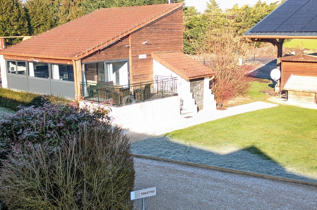 Bâtiment en bois avec terrasse, entouré de pelouse et d'arbustes, sous un ciel dégagé.