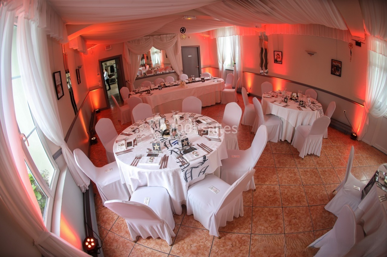 Salle de réception décorée avec des nappes blanches, des chaises couvertes et un éclairage tamisé rouge.