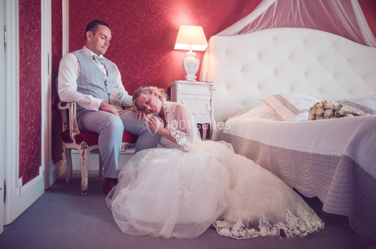Une mariée assise au sol repose sa tête sur les genoux du marié, dans une chambre au décor romantique.
