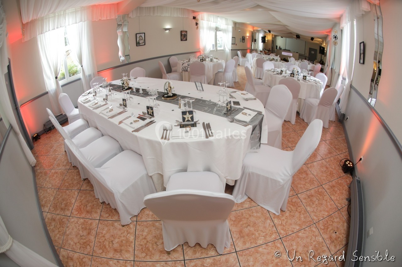 Salle de réception décorée avec des tables rondes et ovales, nappes blanches et chaises assorties.