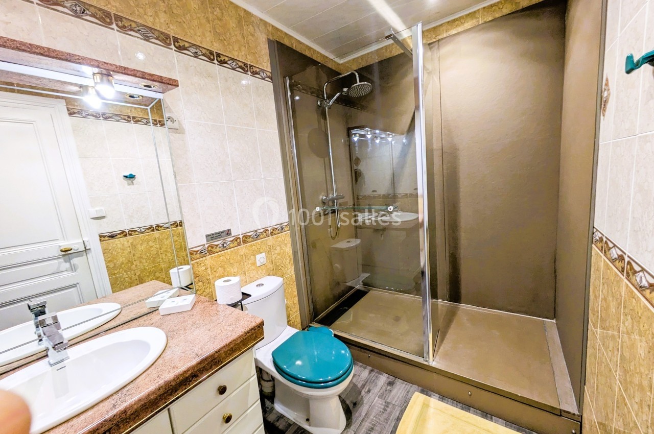 Salle de bain avec douche à l'italienne, lavabo double, toilettes et carrelage beige et marron.