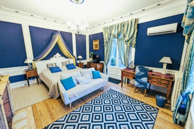 Miniature Location salle Quesmy (Oise) - Château de Quesmy #47 Chambre élégante avec murs bleus, lit double, cheminée, miroir doré, armoire en bois et tapis géométrique.