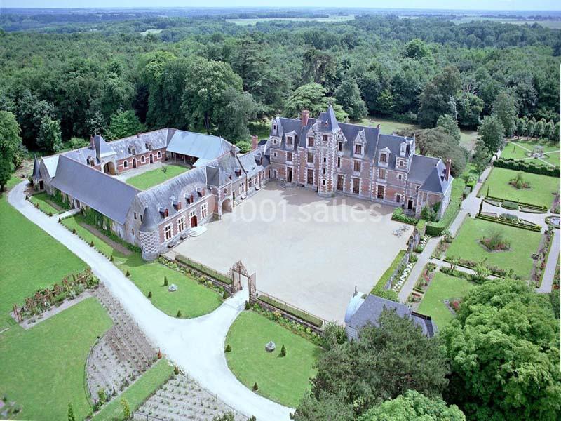 Vue aérienne d'un château entouré de jardins symétriques, d'une cour centrale et de bâtiments annexes.