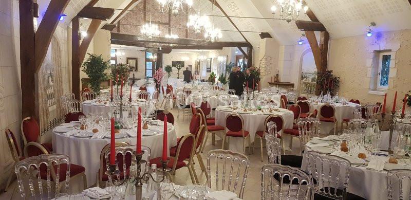 Salle de réception élégante avec tables rondes dressées, chandeliers rouges et décorations lumineuses.