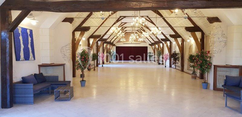 Grande salle lumineuse avec poutres apparentes, lustres, plantes décoratives et un rideau rouge au fond.