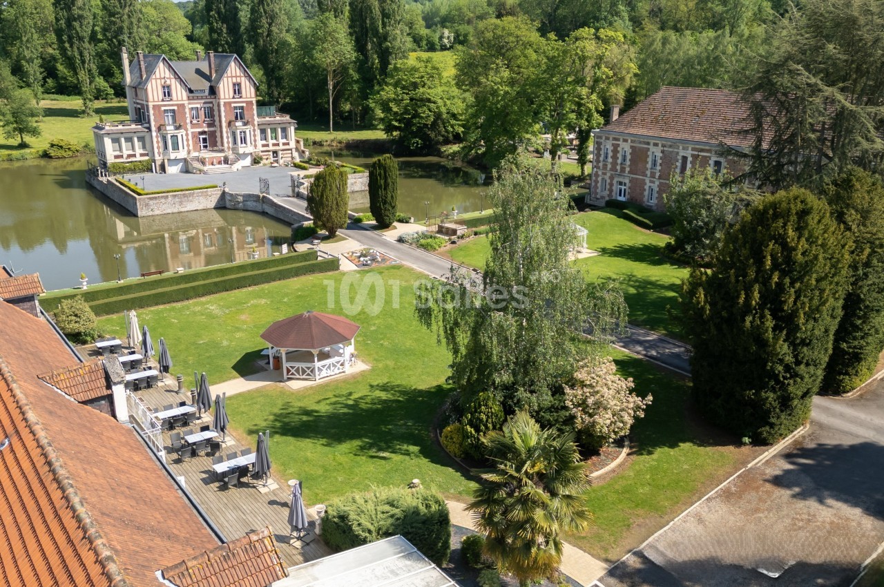 Vue aérienne d'un domaine avec un étang, un bâtiment principal, un kiosque et des jardins arborés.