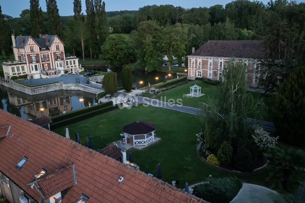 Vue aérienne d'un domaine avec un manoir, un bâtiment en briques, un jardin aménagé et un kiosque au crépuscule.