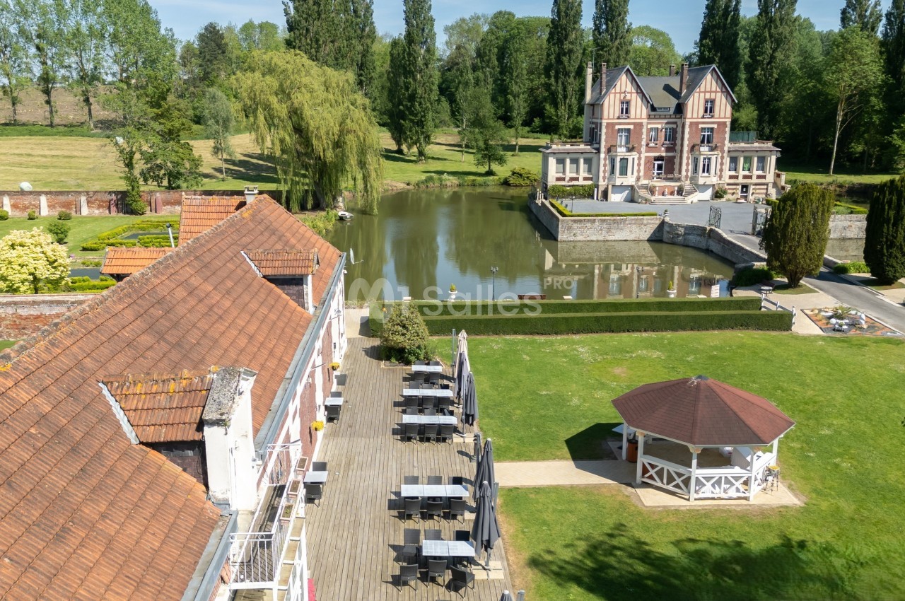 Vue aérienne d'un domaine avec un bâtiment principal au bord d'un étang, une terrasse et un kiosque dans un jardin.