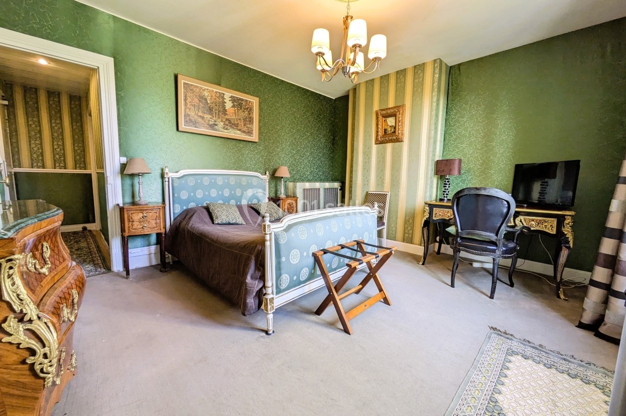 Chambre décorée de style classique avec lit double, meubles anciens, murs verts et un lustre au plafond.