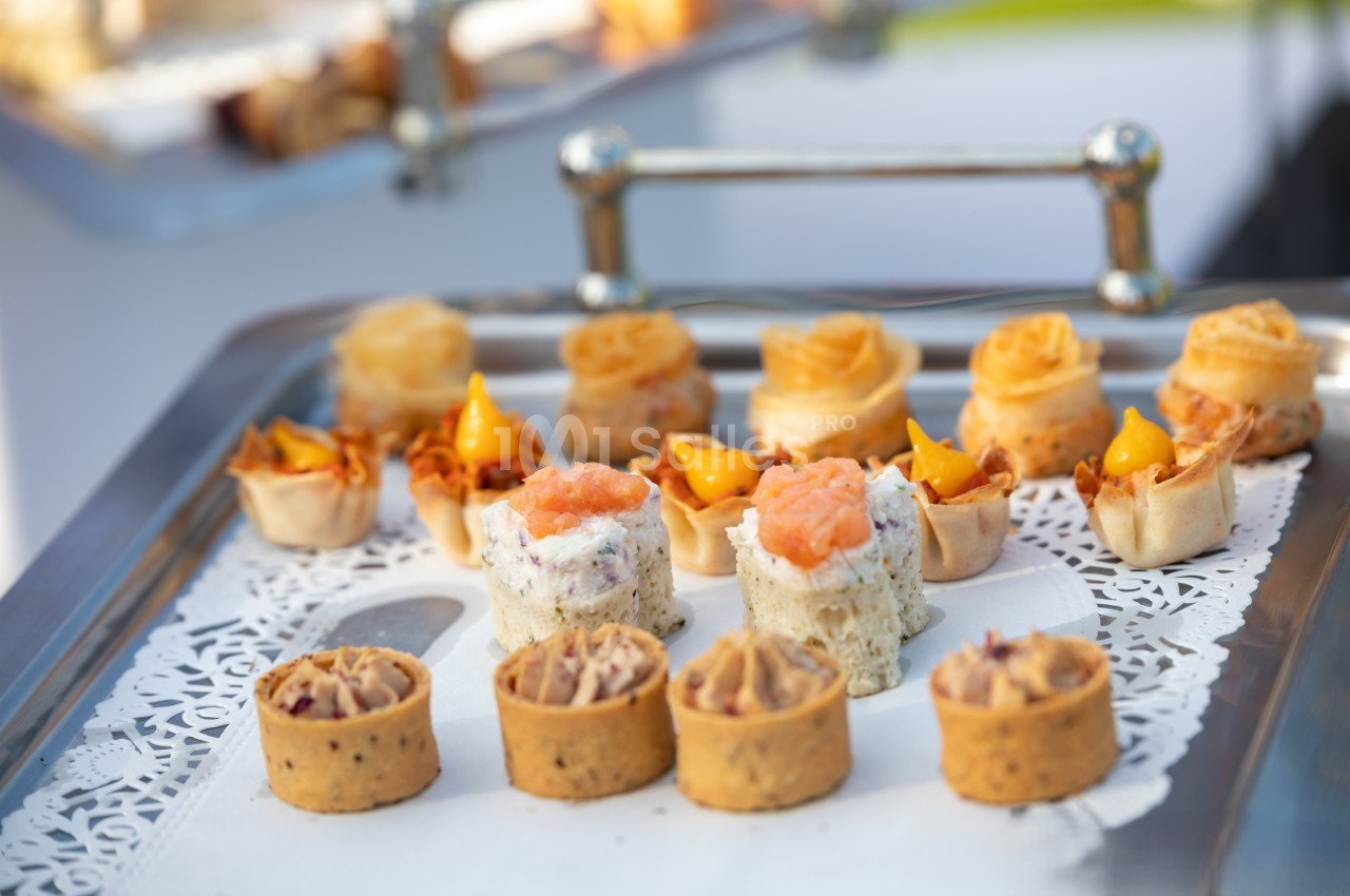 Plateau de petits amuse-bouches variés, présentés sur une nappe en dentelle blanche.