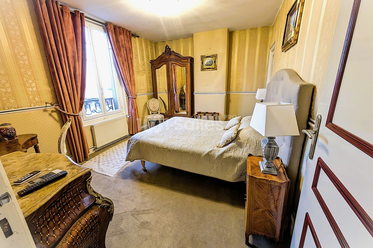 Chambre classique avec lit double, armoire en bois, tapis beige, rideaux épais et lumière naturelle provenant d'une fenêtre.