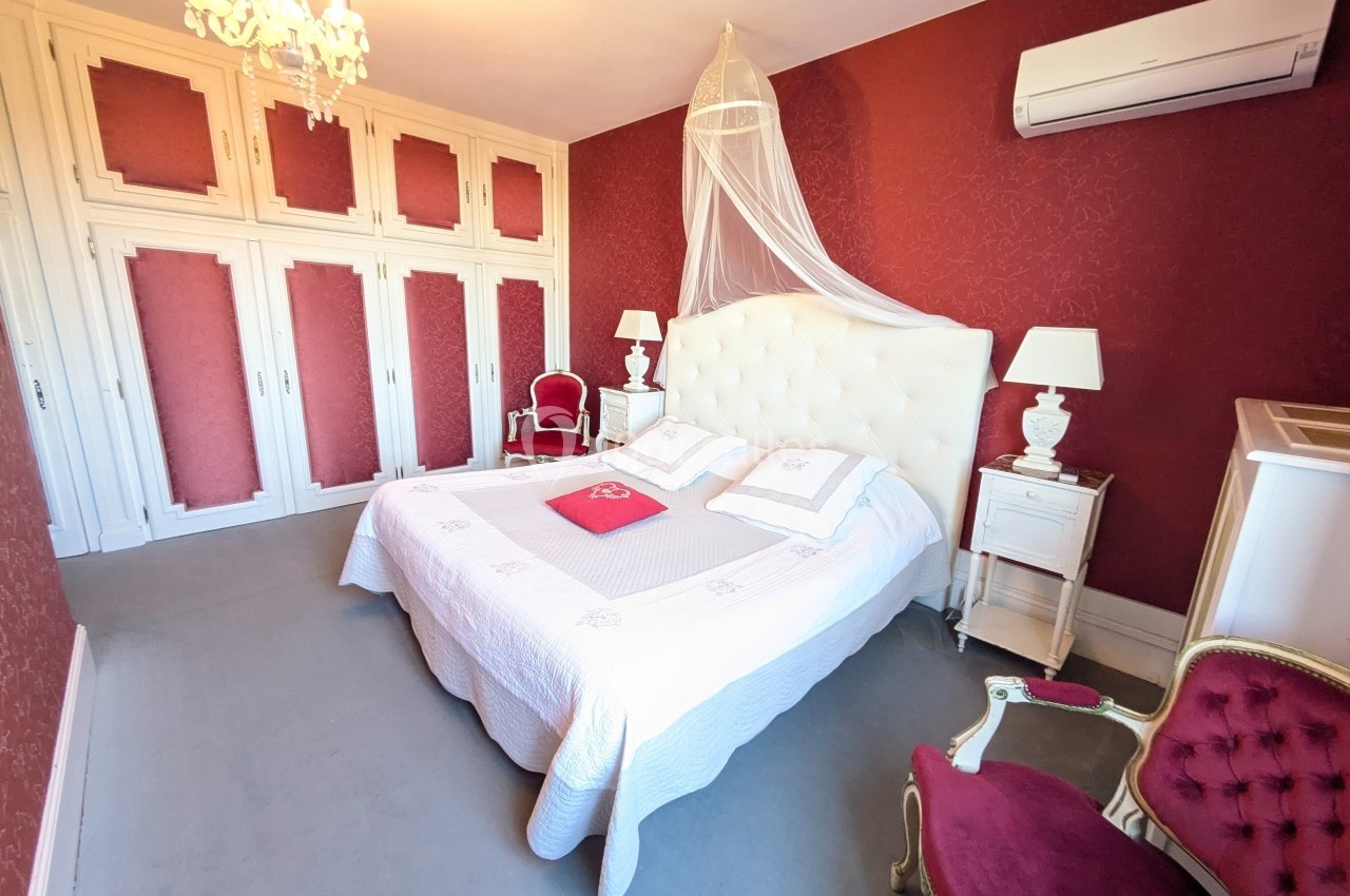 Chambre avec lit double, murs rouges, mobilier classique, armoire intégrée, lustre et climatisation.