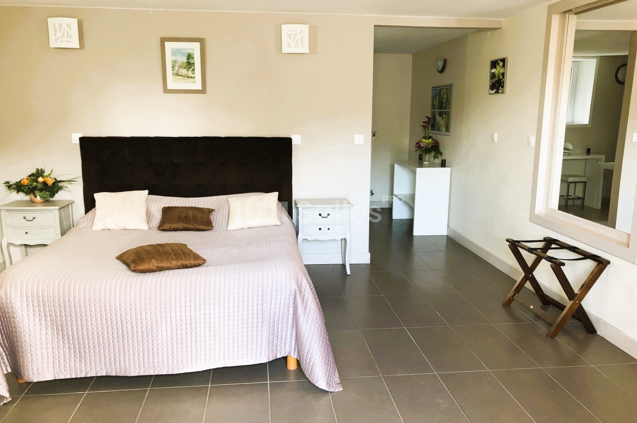 Chambre lumineuse avec lit double, tables de chevet, miroir, décoration murale et sol en carrelage gris.